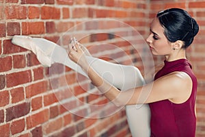 Young ballerina with raised leg tying the ribbon in her shoes