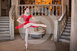 Young ballerina in a red tutu is dancing against background of the theatrical scenery of the palace