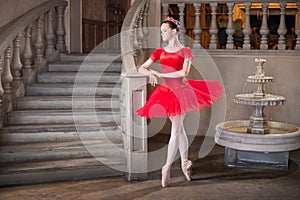 Young ballerina in a red tutu is dancing against background of the theatrical scenery of the palace