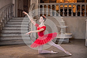 Young ballerina in a red tutu is dancing against background of the theatrical scenery of the palace