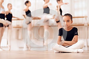 The young ballerina sits on the floor while attending a ballet school.