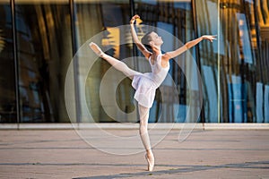 Young ballerina in a white leotard dancing on pointe shoes against the backdrop of cityscape