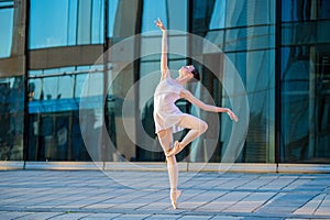 Young ballerina in a white leotard dancing on pointe shoes against the backdrop of cityscape