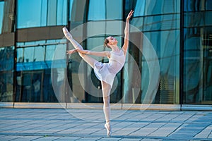Young ballerina in a white leotard dancing on pointe shoes against the backdrop of cityscape
