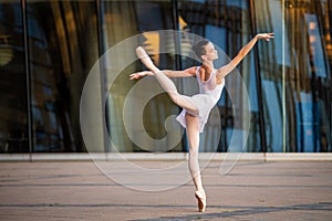 Young ballerina in a white leotard dancing on pointe shoes against the backdrop of cityscape