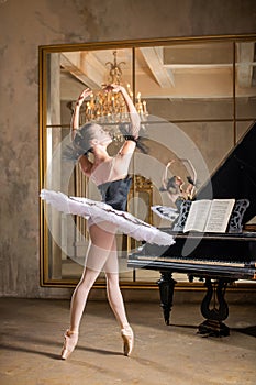 Young ballerina in a white tutu dancing on beautiful old piano in a vintage interior