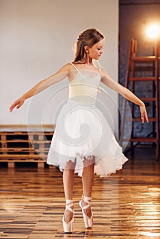 Young ballerina in white tutu practicing dance moves.