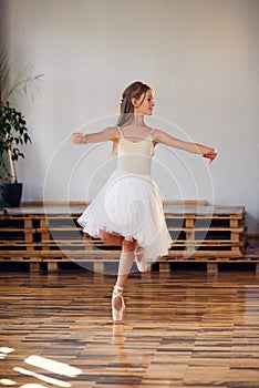 Young ballerina in white tutu practicing dance moves.