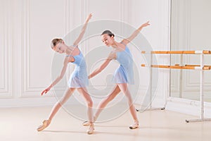 Young ballerinas having rehearsal at studio. Row of happy young ballerinas practicing at ballet barre, focus on first girl