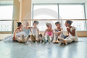 Young ballerinas sitting on floor and embracing.