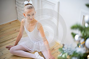 Young ballet dancer sitting near Christmas tree