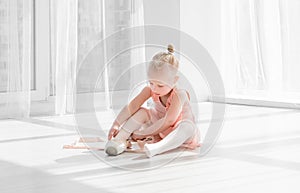 Young ballet dancer in tutu sitting on the floor and tying pointe shoes