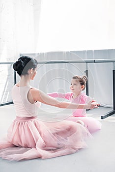 young ballet teacher and little student in pink tutu skirts training together