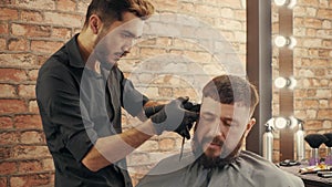 Young barber grooming handsome male client in barbershop