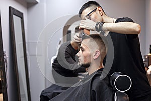 Young barber kazakh works in a barbershop, handsome guy does hair styling for a client with dry gel in a hairdresser