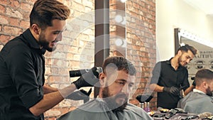 Young barber trimming hair to handsome bearded client in barbershop