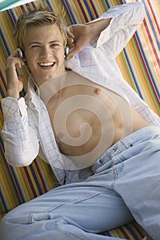 Young bare-chested man on deckchair listening to music on headphones portrait