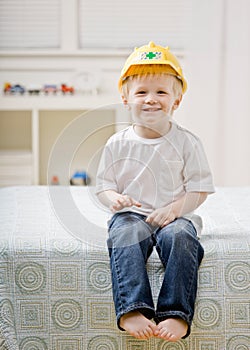 Young barefoot boy sitting on bed in bedroom