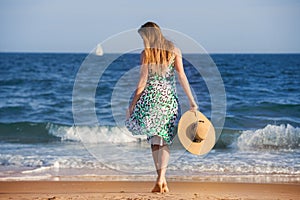Young barefoot woman with hat walking on ocean beach at sunny hot day