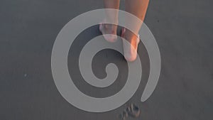 Young barefoot woman legs stepping on wet sand at sea beach in sunset