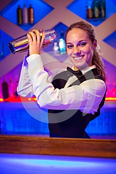 Young barmaid with cocktail shaker at counter