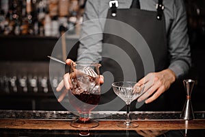 Young barman making a fresh alcoholic cocktail into the cocktail glass