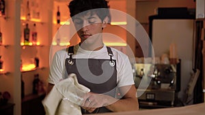 Young barman polishing the wine glass in cafe bar