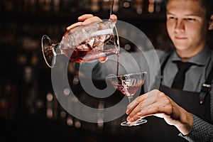 Young barman pouring a fresh alcoholic cocktail into the cocktail glass