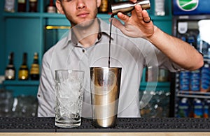 Young Barman`s making cocktail, pouring alcohol into glass