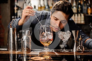 Young barman stirring fresh alcoholic cocktail with syrups