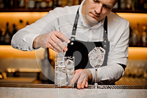 Young barman stirring ice cubes in a glass