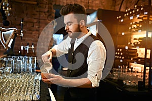 Young barmen concentrated on pouring milk to coffee