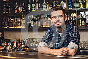 Young bartender leaning on bar counter smiling restrained