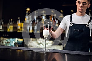 A young bartender pours champagne into a glass from a bottle on the bar