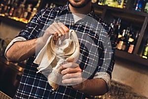 Young bartender standing at bar counter cleaning glass with tissue close-up