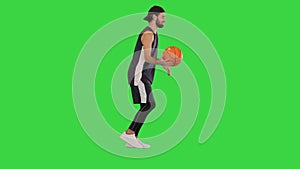 Young basketball player dribbling the ball while walking on a Green Screen, Chroma Key.