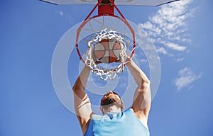 Young basketball player dunking basketball on outdoor court.