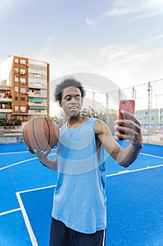 Young basketball player taking a selfie holding the ball in the street basketball court