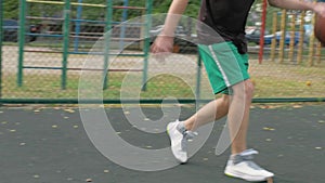 Young basketball player training with ball on basketball court outdoors.