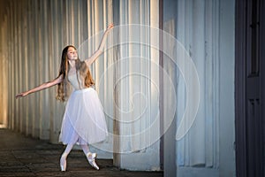 Young bayerina in a long white skirt stands in a graceful pose on pointes