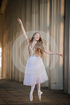 Young bayerina in a long white skirt stands in a graceful pose on pointes