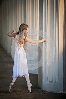 Young bayerina in a long white skirt stands in a graceful pose on pointes