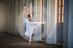 Young bayerina in a long white skirt stands in a graceful pose on pointes