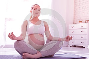 Young beaming long-haired pregnant woman in a white t-shirt looking peaceful