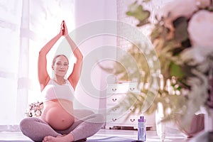 Young beaming long-haired pregnant woman in a white t-shirt looking peaceful