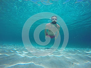 Young beard man with glasses diving in a blue clean water