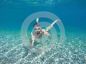 Young beard man with mask diving in a clean water