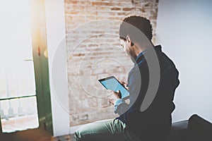 Young bearded African man using laptop while sitting on sofa at his modern home office.Concept of people working with