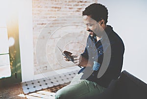 Young bearded African man using laptop while sitting on sofa at his modern home office.Concept of people working with