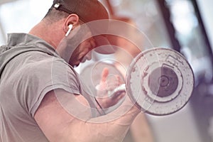 Young bearded athlete man in earpieces and cap lifting heavy weight in sport gym with hard effort photo